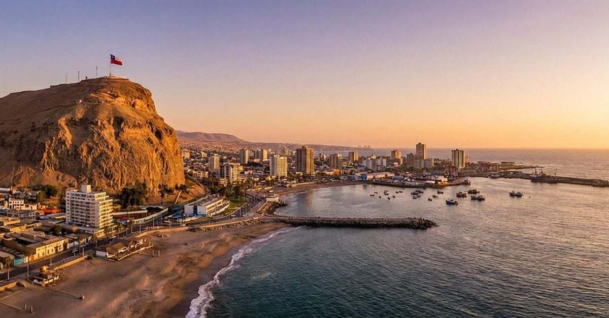 El Morro de Arica con la bandera chilena sobre la ciudad y el puerto al atardecer.