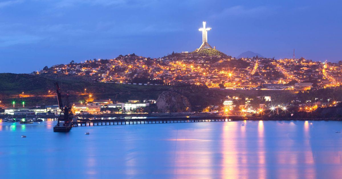 La Cruz del Tercer Milenio iluminada sobre Coquimbo, con la bahía y el muelle al anochecer.