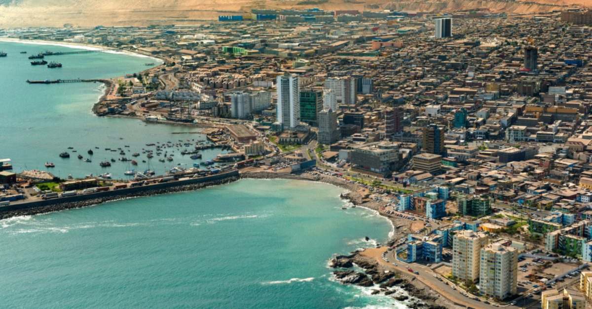 Vista aérea de Iquique: la bahía con embarcaciones, la ciudad y el cerro del desierto al fondo.